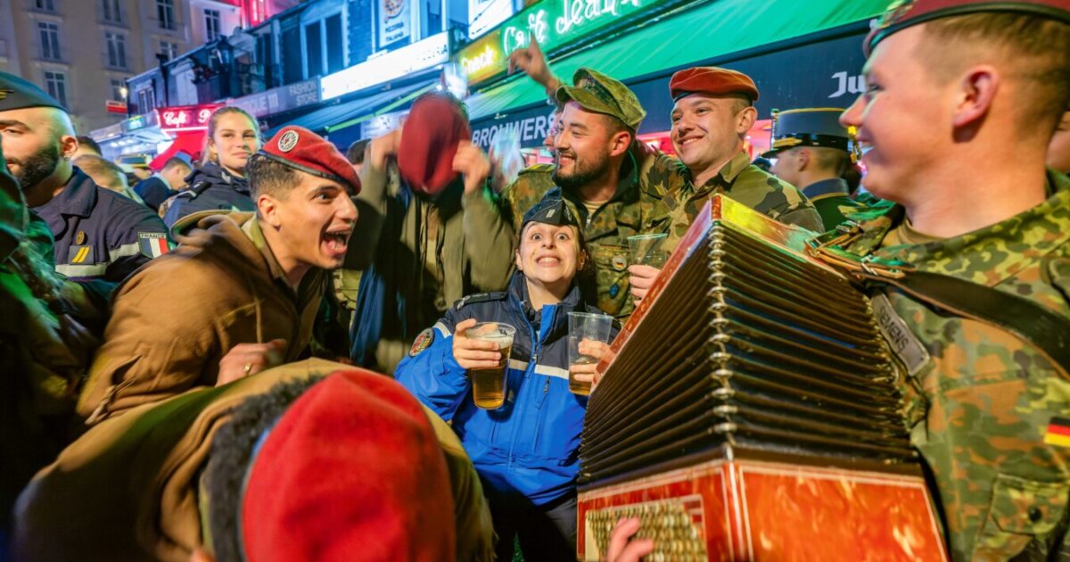 Eine Gruppe feiernder Soldaten in verschiedenen Uniformen, einer spielt Akkordeon