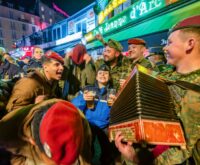 Eine Gruppe feiernder Soldaten in verschiedenen Uniformen, einer spielt Akkordeon