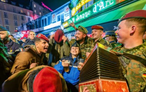 Eine Gruppe feiernder Soldaten in verschiedenen Uniformen, einer spielt Akkordeon