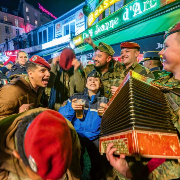 Eine Gruppe feiernder Soldaten in verschiedenen Uniformen, einer spielt Akkordeon