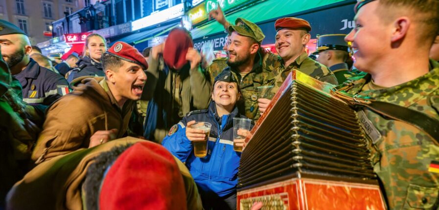 Eine Gruppe feiernder Soldaten in verschiedenen Uniformen, einer spielt Akkordeon