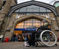 Ein Mann im Bundeswehrparka sitzt vor dem Hauptbahnhof in einem Rollstuhl
