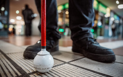 Füße und ein Taststock stehen auf einem Leitstreifen