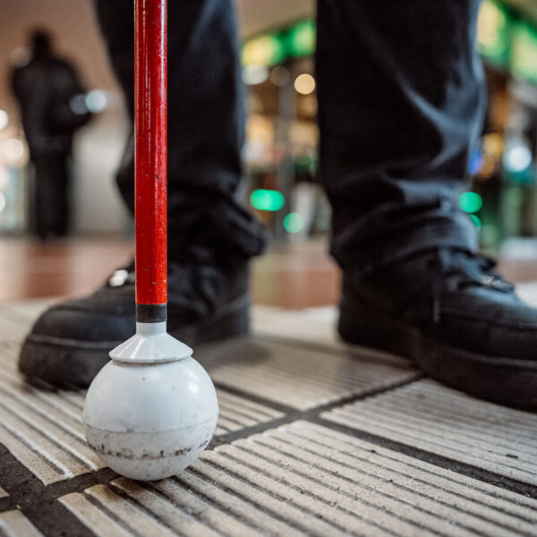 Füße und ein Taststock stehen auf einem Leitstreifen