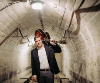 Ein Mann mit einer Gitarre auf der Schulter geht durch einen Tunnel