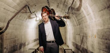 Ein Mann mit einer Gitarre auf der Schulter geht durch einen Tunnel