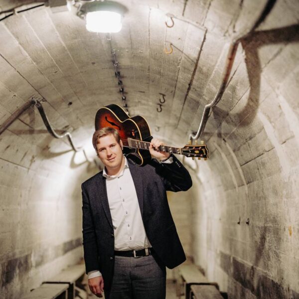 Ein Mann mit einer Gitarre auf der Schulter geht durch einen Tunnel