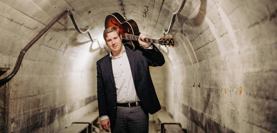 Ein Mann mit einer Gitarre auf der Schulter geht durch einen Tunnel