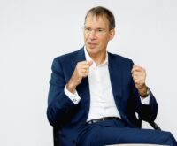 Ein Mann in dunkelblauem Anzug und weißem Hemd gestikuliert