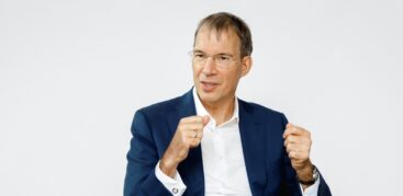 Ein Mann in dunkelblauem Anzug und weißem Hemd gestikuliert