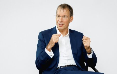 Ein Mann in dunkelblauem Anzug und weißem Hemd gestikuliert