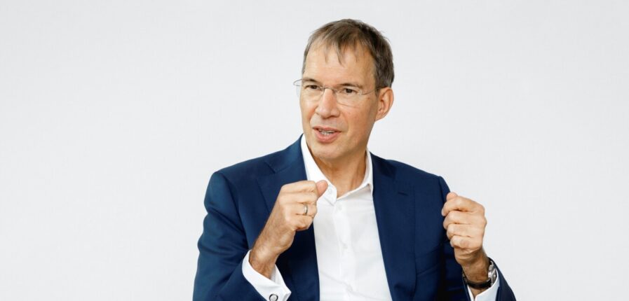 Ein Mann in dunkelblauem Anzug und weißem Hemd gestikuliert