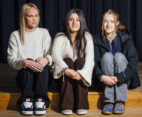 Drei Mädchen sitzen auf einer Stufe vor einem dunklen Vorhang.