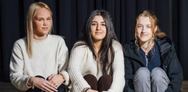 Drei Mädchen sitzen auf einer Stufe vor einem dunklen Vorhang.