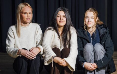 Drei Mädchen sitzen auf einer Stufe vor einem dunklen Vorhang.