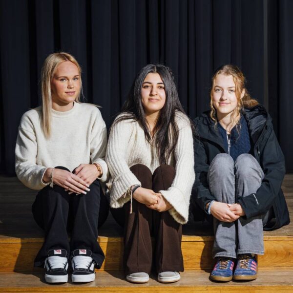 Drei Mädchen sitzen auf einer Stufe vor einem dunklen Vorhang.