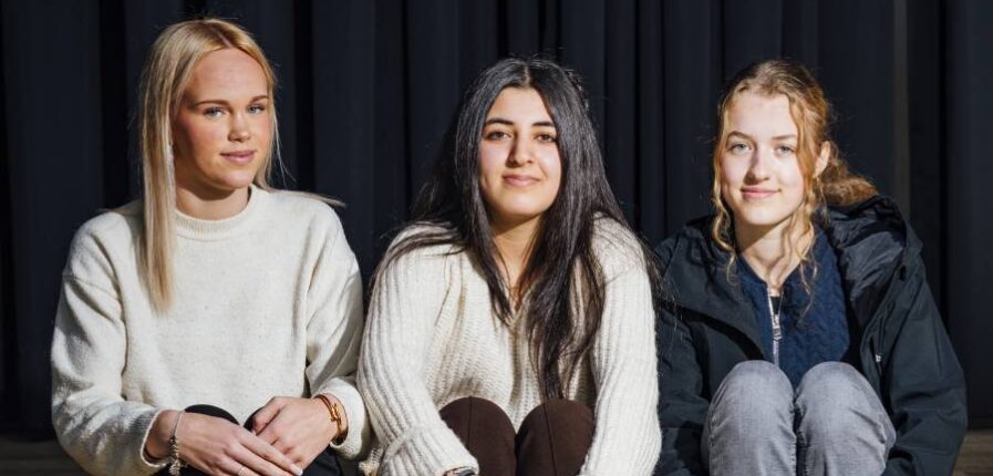 Drei Mädchen sitzen auf einer Stufe vor einem dunklen Vorhang.