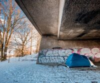 Ein blaues Zelt steht unter einer Betonbrücke aus schneebedeckten Boden. Foto: Mauricio Bustamante