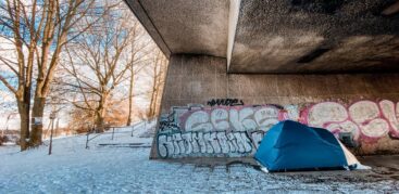 Ein blaues Zelt steht unter einer Betonbrücke aus schneebedeckten Boden. Foto: Mauricio Bustamante