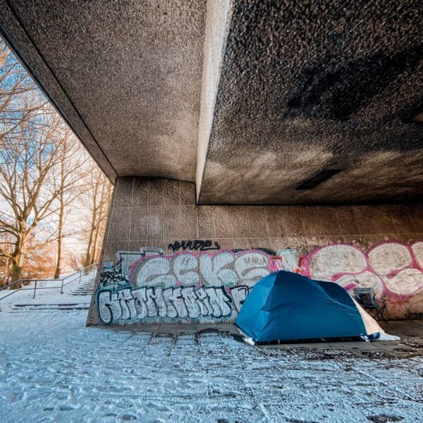 Ein blaues Zelt steht unter einer Betonbrücke aus schneebedeckten Boden. Foto: Mauricio Bustamante