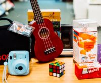 Eine Ukulele, ein Zauberwürfel und andere Dinge vor einem Schild mit der Aufschrift "Bibliothek der Dinge"