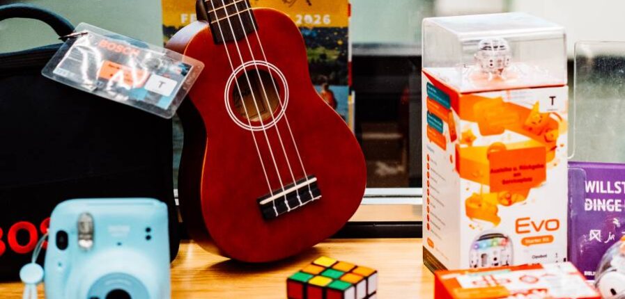 Eine Ukulele, ein Zauberwürfel und andere Dinge vor einem Schild mit der Aufschrift "Bibliothek der Dinge"