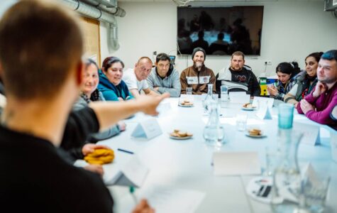 Eine Gruppe von Menschen sitzt an einem Tisch, alle schauen zum Mann am Tischkopf