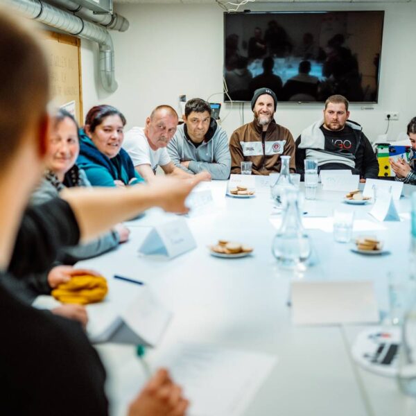 Eine Gruppe von Menschen sitzt an einem Tisch, alle schauen zum Mann am Tischkopf