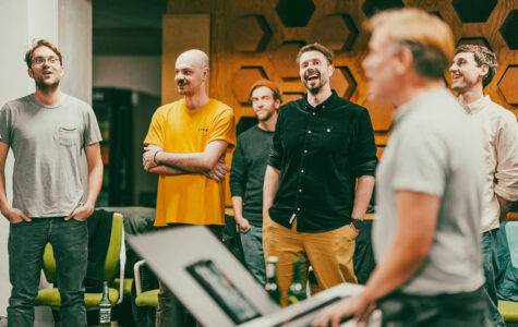 Vier Männer stehen in einem Raum und singen, einer spielt Keyboard