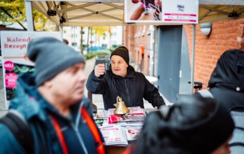 Ein Mann mit Mütze steht hinter einem Tresen vor einem Backsteinhaus