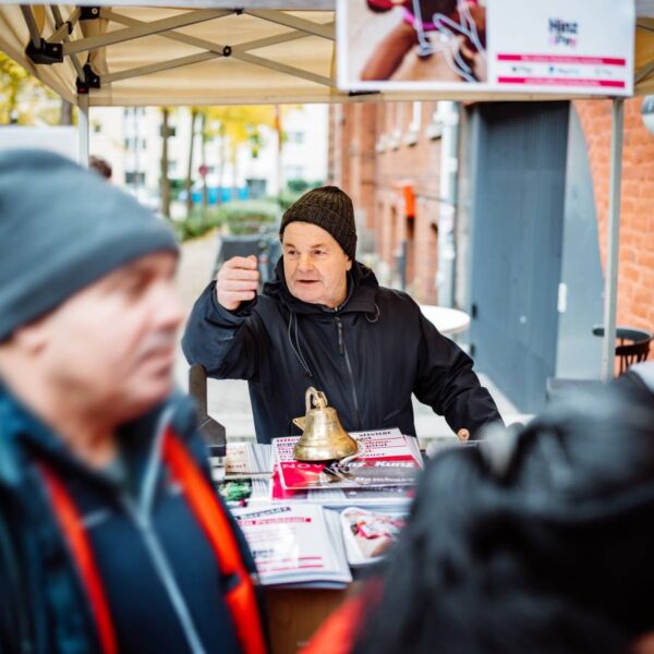 Ein Mann mit Mütze steht hinter einem Tresen vor einem Backsteinhaus