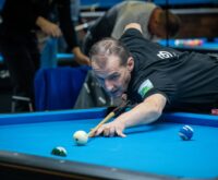 Ein Mann lehnt vornüber auf einem Billiardtisch und zielt mit dem Queue auf eine Kugel