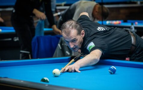 Ein Mann lehnt vornüber auf einem Billiardtisch und zielt mit dem Queue auf eine Kugel