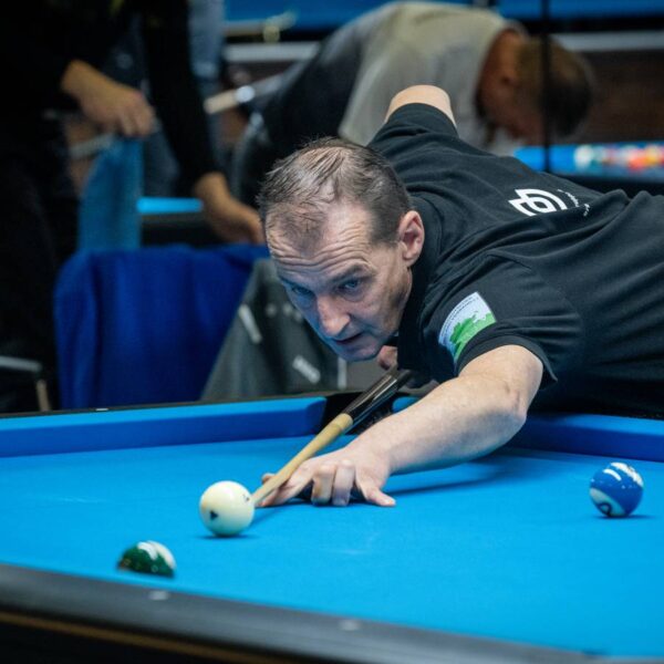 Ein Mann lehnt vornüber auf einem Billiardtisch und zielt mit dem Queue auf eine Kugel