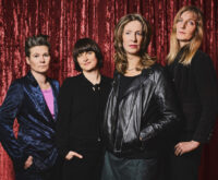 Vier Frauen stehen vor einem roten Vorhang und schauen ernst in die Kamera