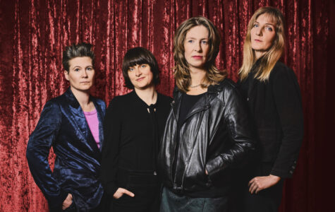 Vier Frauen stehen vor einem roten Vorhang und schauen ernst in die Kamera