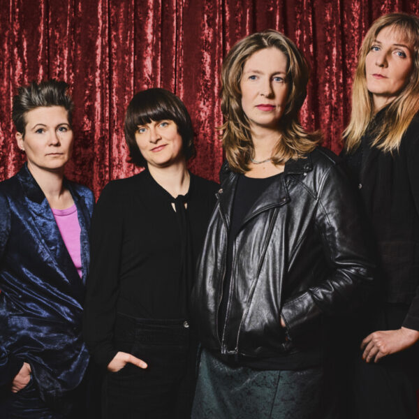 Vier Frauen stehen vor einem roten Vorhang und schauen ernst in die Kamera