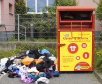 Ein Altkleidercontainer. Daneben liegt ein Haufen Klamotten auf der Erde.