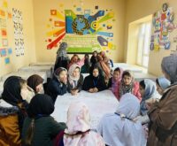 Mädchen mit Kopftuch sitzen im Kreis um einen Tisch herum