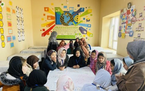 Mädchen mit Kopftuch sitzen im Kreis um einen Tisch herum