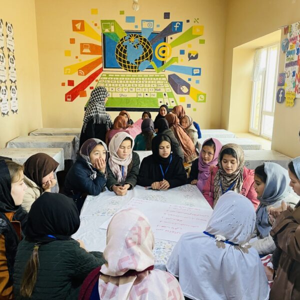 Mädchen mit Kopftuch sitzen im Kreis um einen Tisch herum