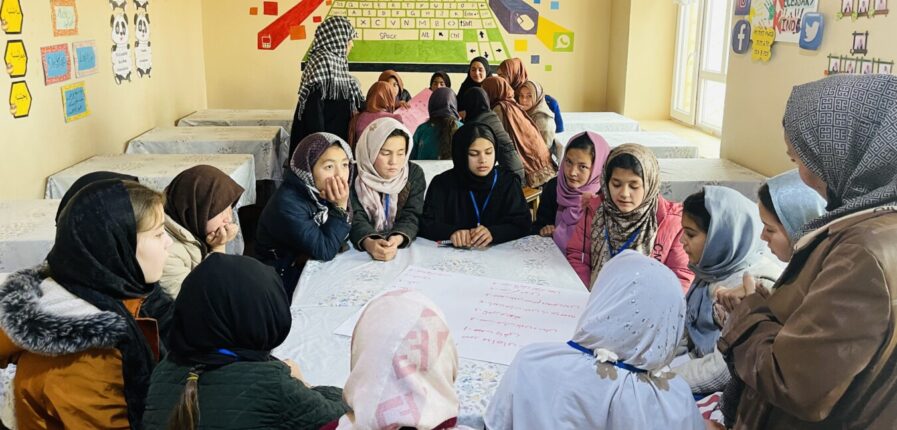 Mädchen mit Kopftuch sitzen im Kreis um einen Tisch herum