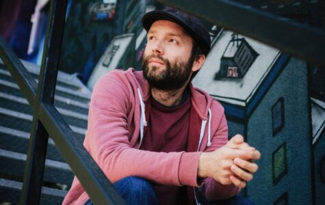 Ein Mann mit Vollbart, Mütze und im Hoodie sitzt auf einer Treppe