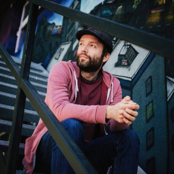 Ein Mann mit Vollbart, Mütze und im Hoodie sitzt auf einer Treppe