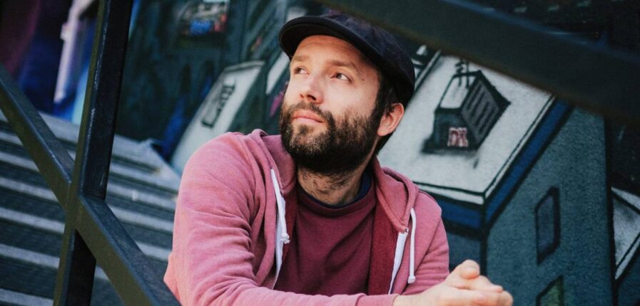 Ein Mann mit Vollbart, Mütze und im Hoodie sitzt auf einer Treppe