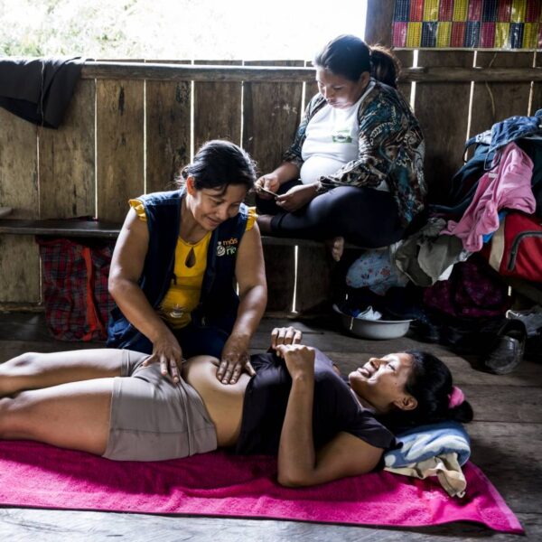 Eine schwangere Frau liegt rücklings auf dem Boden, eine andere kniet neben ihr und tastet den Bauch ab