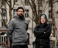 Ein Mann mit Mütze und eine Frau mit grünen Haaren schauen in die Kamera