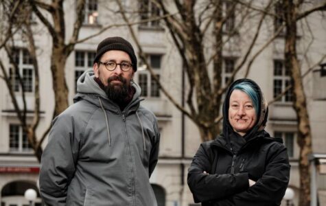 Ein Mann mit Mütze und eine Frau mit grünen Haaren schauen in die Kamera