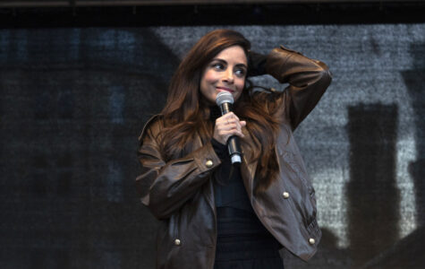 Eine Frau mit braunen Haaren und brauner Lederjacke hält ein Mikrofon in der Hand