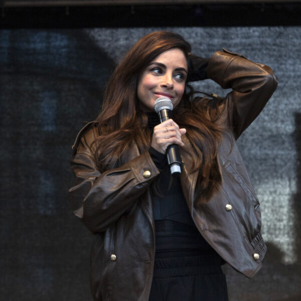 Eine Frau mit braunen Haaren und brauner Lederjacke hält ein Mikrofon in der Hand